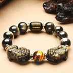 Black gold obsidian grounding bracelet with tiger eye accent photographed in a warm neutral setting.