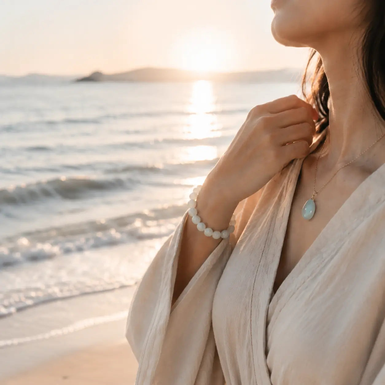 Mariv Stones natural gemstone jewelry lifestyle photo - calm beach sunset with jade bracelet and teardrop necklace.