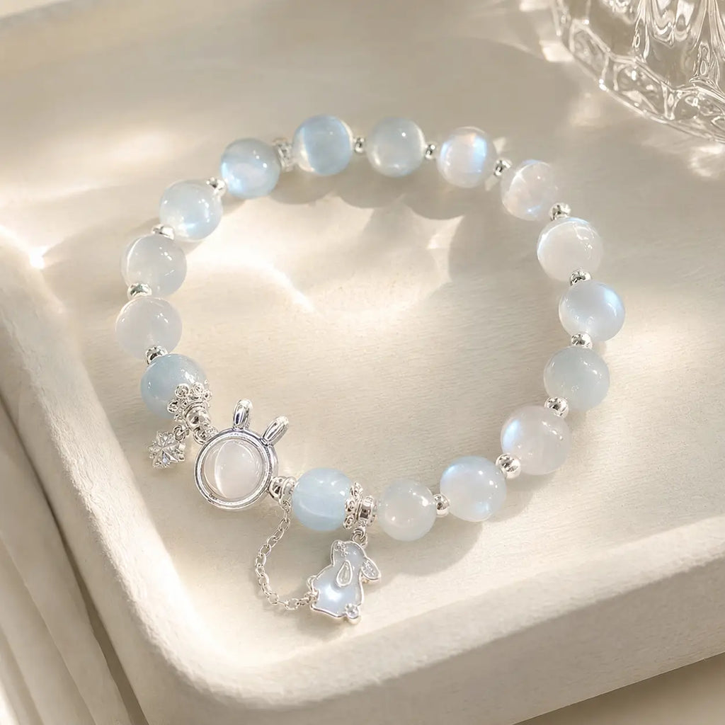 Blue glow moonstone bracelet with dainty rabbit charm on white stand.