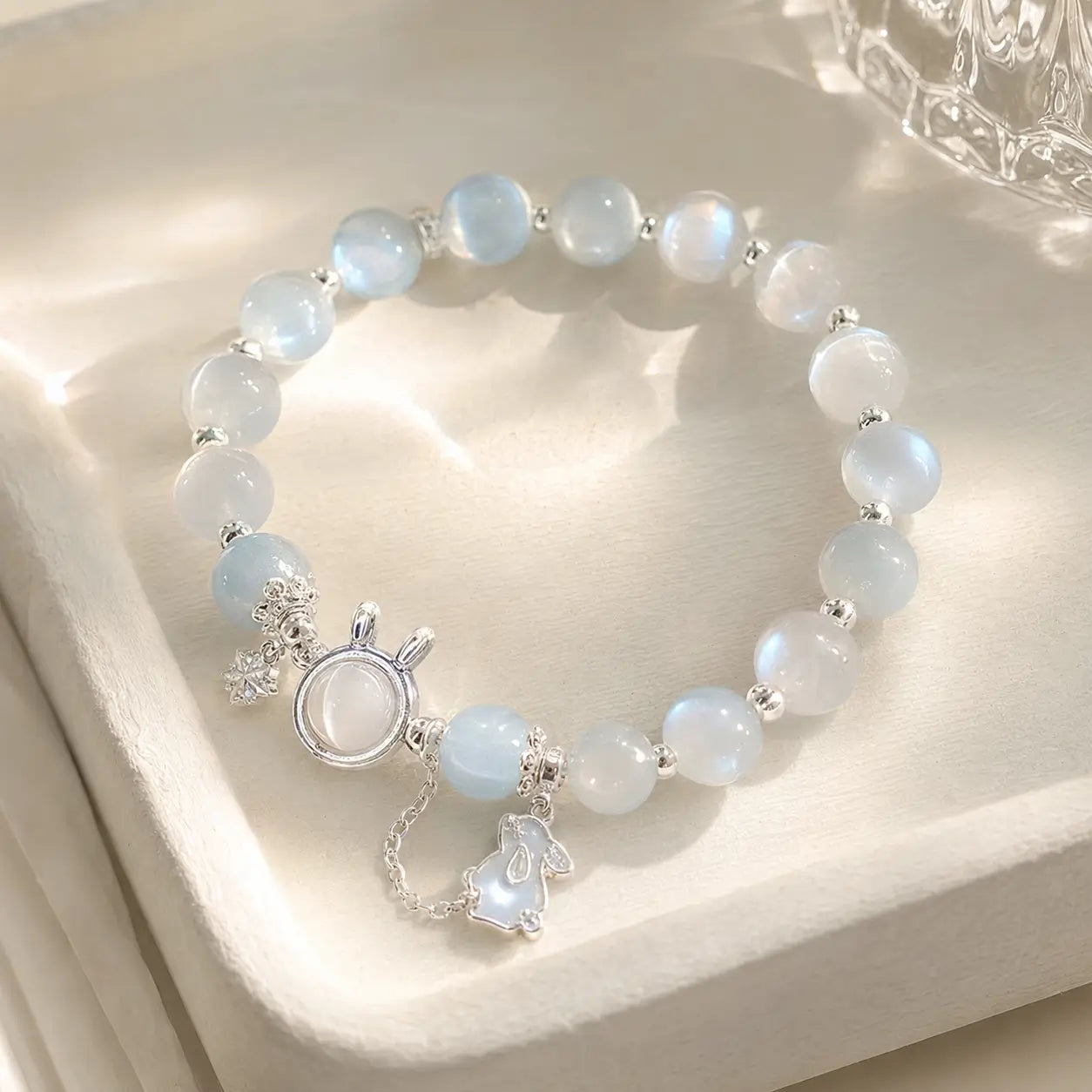 Blue glow moonstone bracelet with dainty rabbit charm on white stand.