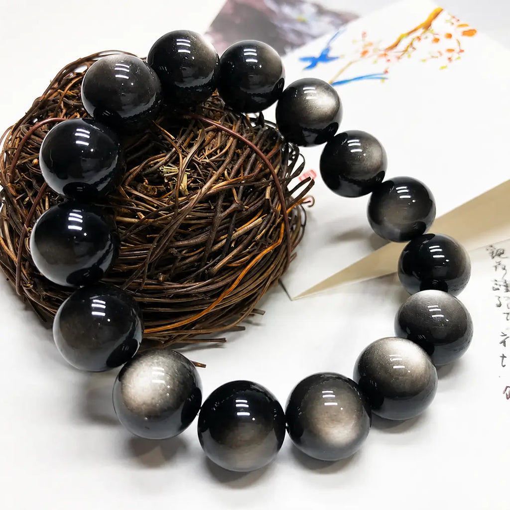 Natural Silver Sheen Obsidian Bracelet displayed with woven decor, featuring reflective gemstone beads and grounding energy.